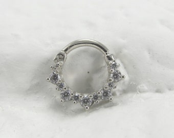 May include: A silver clicker ring with a row of clear cubic zirconia stones around the edge.