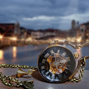 May include: A gold pocket watch with a black face and Roman numeral markings. The watch has a skeletonized design, revealing the intricate gears and mechanics inside. The watch is attached to a gold chain.