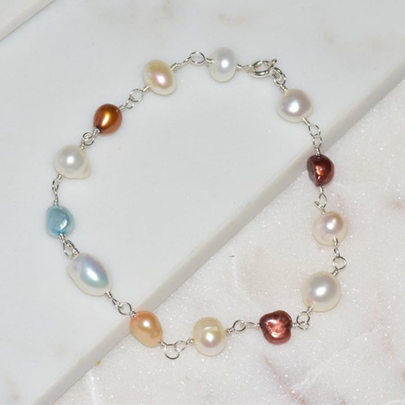 May include: A delicate pearl bracelet with a silver chain and a variety of colored pearls, including white, cream, light blue, brown, and red.