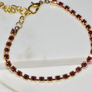 May include: A gold chain bracelet with a row of small, square, pink rhinestones.