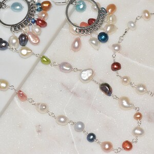 May include: A silver chain necklace with a variety of pearl and gemstone beads. The necklace features a mix of white, pink, and blue pearls, as well as green, red, and blue gemstones.