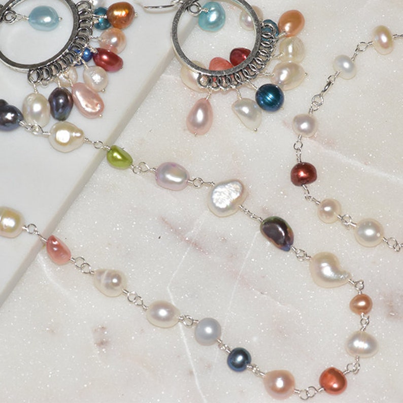May include: A silver chain necklace with a variety of pearl and gemstone beads. The necklace features a mix of white, pink, and blue pearls, as well as green, red, and blue gemstones.