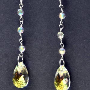 May include: A pair of silver dangle earrings with iridescent beads and teardrop-shaped crystals. The crystals are a pale yellow color.