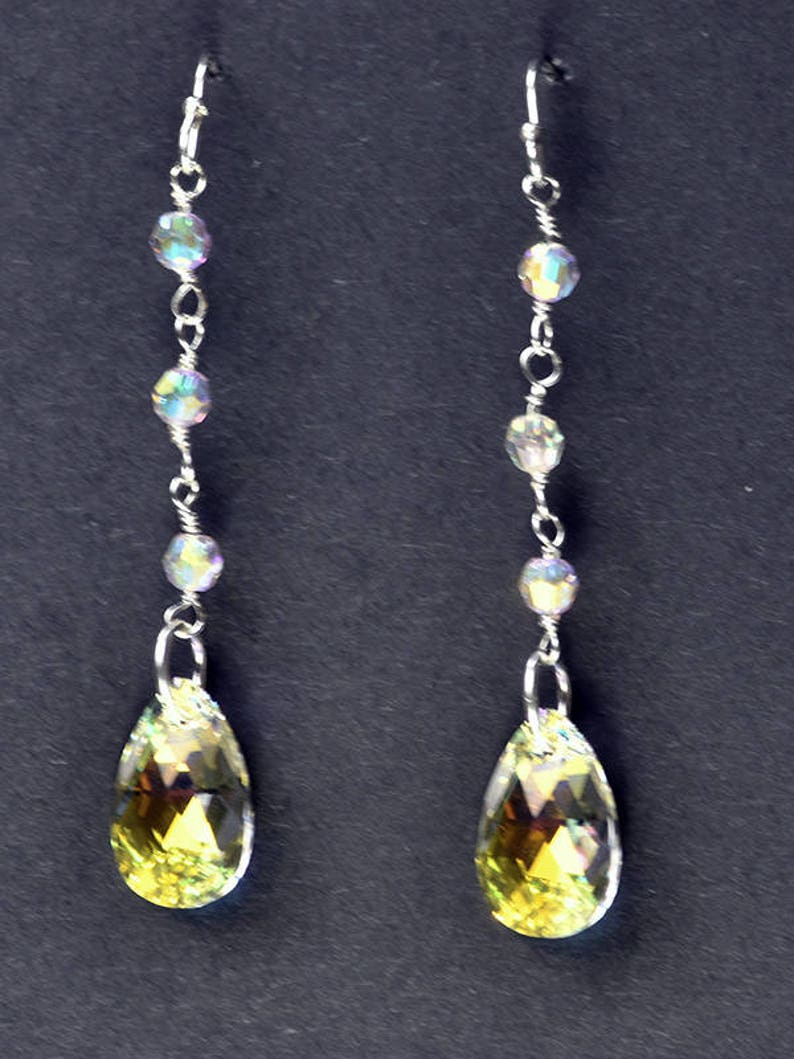 May include: A pair of silver dangle earrings with iridescent beads and teardrop-shaped crystals. The crystals are a pale yellow color.