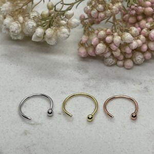 May include: Three nose rings with a ball end. The rings are silver, gold, and rose gold.
