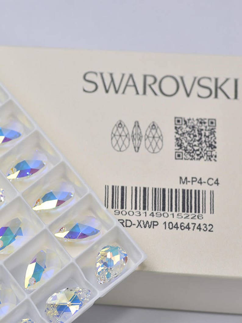May include: A white box with the Swarovski logo and a barcode. The box contains a clear plastic tray with 12 crystal teardrop pendants.