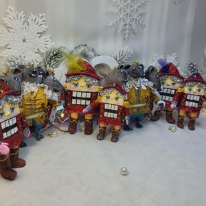 Pode incluir: Uma coleção de enfeites de Natal feitos à mão com figuras de quebra-nozes e ratos. Os quebra-nozes usam jaquetas e chapéus vermelhos, enquanto os ratos usam trajes amarelos e dourados. Os enfeites têm traços faciais detalhados e estão em uma superfície branca.