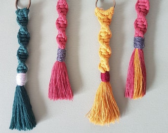 May include: Four colorful macrame keychains with tassels. The keychains are green, pink, yellow, and red. Each keychain has a silver metal ring.