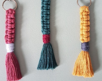 May include: Three colorful macrame keychains with tassels. The keychains are made with red, green, and yellow yarn. Each keychain has a silver metal ring and a silver metal clasp.