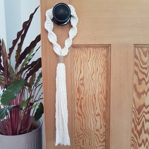 May include: A white macrame doorstop with a tassel hanging from a wooden door.
