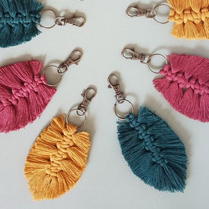 May include: Five colorful leaf-shaped keychains with silver key rings. The keychains are made of yarn and have a fringe detail. The colors are teal, pink, yellow, and a darker teal.