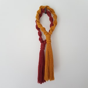 May include: A macrame wall hanging with two tassels, one red and one yellow.