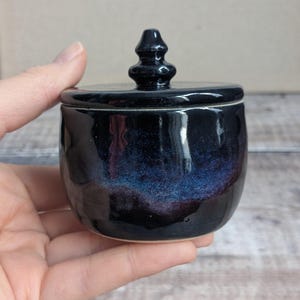 Small ceramic lidded pot with a black glaze and blue and purple hints