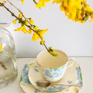 K&ouml;nnte beinhalten: Ein wei&szlig;es Tee-Set mit einem blauen Blumenmuster. Das Set befindet sich auf einer wei&szlig;en Oberfl&auml;che mit einem Zweig gelber Blumen.