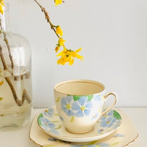 K&ouml;nnte beinhalten: Ein Vintage-Teetassen- und Untertassen-Set mit Blumenmuster. Tasse und Untertasse sind wei&szlig; mit blauen und gr&uuml;nen Blumen. Die Untertasse hat einen gewellten Rand.
