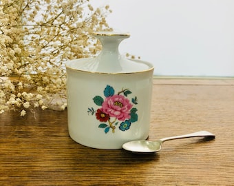 Könnte beinhalten: Weiße Zuckerdose aus Keramik mit einem Blumendesign in Rosa, Rot, Blau und Grün. Die Schale hat einen goldenen Rand und wird mit einem passenden Löffel geliefert.