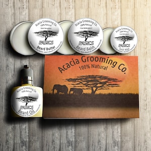 Puede incluir: Un conjunto de productos para el cuidado de la barba de Acacia Grooming Co. El conjunto incluye mantequilla para barba, bálsamo para barba y cera para el bigote. Los productos son 100% naturales y vienen en pequeñas latas de metal. El conjunto está empaquetado en una caja con una escena de puesta de sol y elefantes.