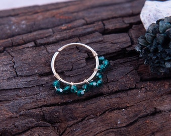 May include: A gold hoop earring with a row of emerald green crystals dangling from the bottom.