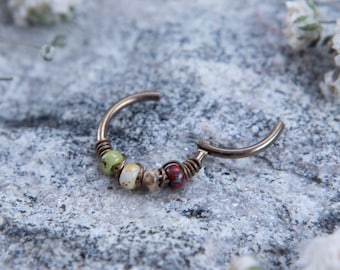 May include: A silver hoop earring with a row of colorful beads. The beads are green, white, brown, and red.