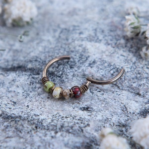 May include: A silver hoop earring with a row of colorful beads. The beads are green, white, brown, and red.