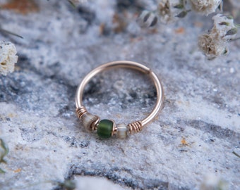 May include: A gold hoop nose ring with a green glass bead and smaller white beads.