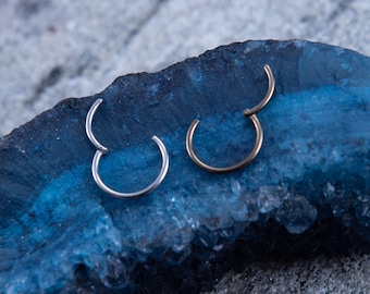 May include: Two small hoop earrings, one silver and one gold, are displayed on a blue and white crystal rock.