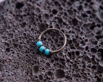 May include: A silver hoop nose ring with three turquoise beads.