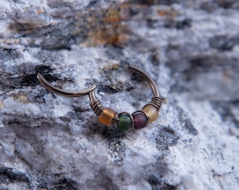 May include: A silver hoop earring with four small, colorful glass beads. The beads are yellow, green, purple, and yellow.