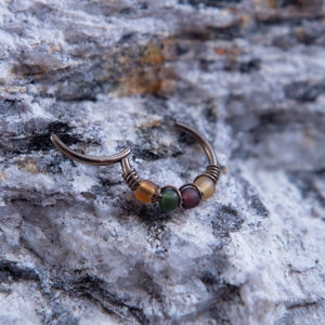May include: A silver hoop earring with four small, colorful glass beads. The beads are yellow, green, purple, and yellow.