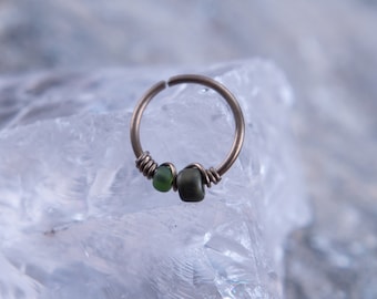 May include: A silver hoop nose ring with two small green glass beads.