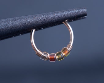 May include: A gold hoop earring with a row of colorful glass beads. The beads are in shades of brown, orange, yellow, and green.