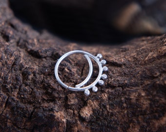 May include: A silver nose ring with a small circle and a row of small beads on the top half of the circle.