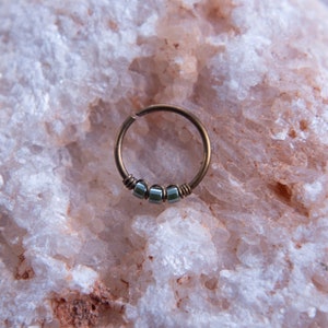 May include: A gold hoop earring with a row of four small, square, iridescent green beads.