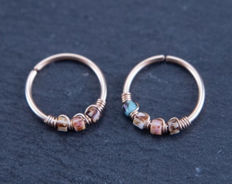 May include: Two gold hoop earrings with small, colorful beads. The beads are a mix of brown, white, and pink.