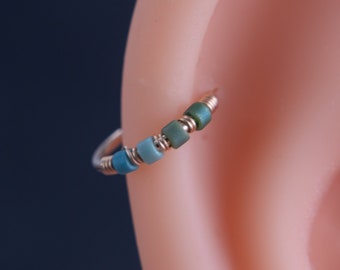 May include: A close-up of a silver hoop earring with blue and green beads. The earring is worn in a person's ear.