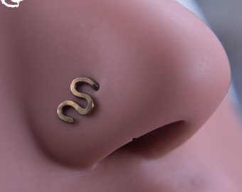 May include: A gold-colored nose ring in the shape of the letter 'S'. The ring is 20 gauge.