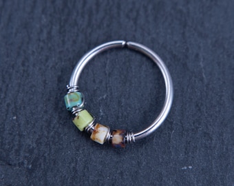 May include: A silver hoop nose ring with four colourful glass beads. The beads are turquoise, green, brown and white.