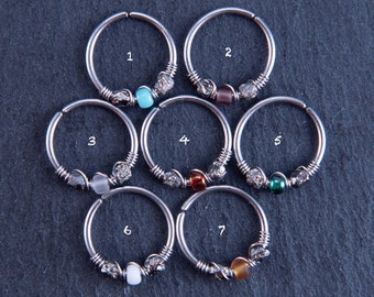 May include: Seven silver hoop earrings with different colored beads. The beads are turquoise, purple, white, red, green, white, and brown.