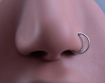 May include: A silver nose ring with a twisted wire design. The ring is worn in a person's left nostril.