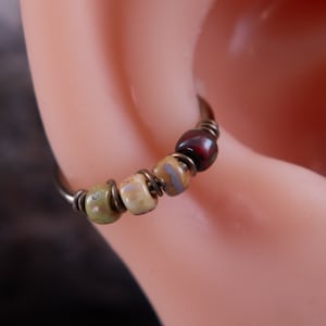 May include: A close-up of a hoop earring with a wire wrapped around it. The hoop is adorned with four small, colorful beads. The beads are green, beige, and red.