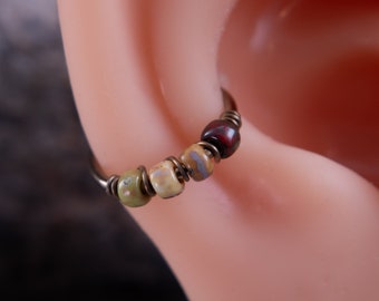 May include: A close-up of a hoop earring with a wire wrapped around it. The hoop is adorned with four small, colorful beads. The beads are green, beige, and red.