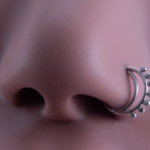 May include: A silver nose ring with a double hoop design and a row of small beads around the top hoop.