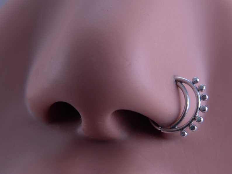 May include: A silver nose ring with a double hoop design and a row of small beads around the top hoop.