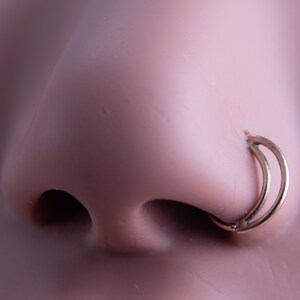 May include: A gold nose ring with a double hoop design. The ring is worn in a person's left nostril.