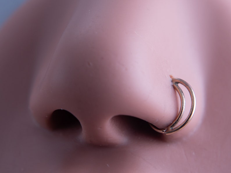 May include: A gold nose ring with a double hoop design. The ring is worn in a person's left nostril.