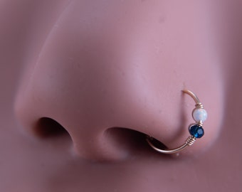 May include: A gold nose ring with a white opal and a dark blue gemstone.