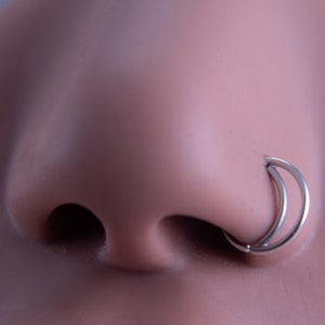 May include: A silver double hoop nose ring. The ring is made of two hoops that are connected together.