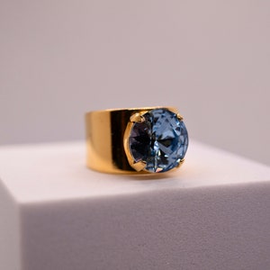 May include: A gold ring featuring a large, round, light blue gemstone.