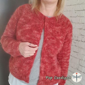Könnte beinhalten: Ein rot-weiß gestrickter Cardigan mit schlichtem Design. Der Cardigan hat einen Knopfleistenverschluss und lange Ärmel. Der Text "Pop Cardigan" ist auf dem Bild zu sehen.