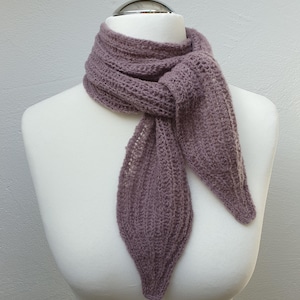 May include: A mauve knitted scarf is displayed on a white mannequin. The scarf has a textured pattern and leaf-shaped ends. It is knotted at the neck, highlighting its design. The scarf's colour and style are suitable for various outfits.